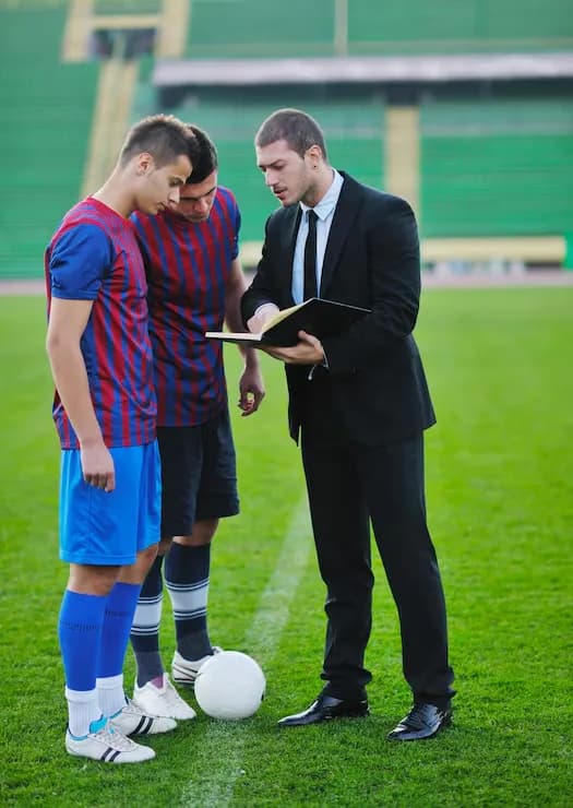 A coach reviewing notes with two players on the field